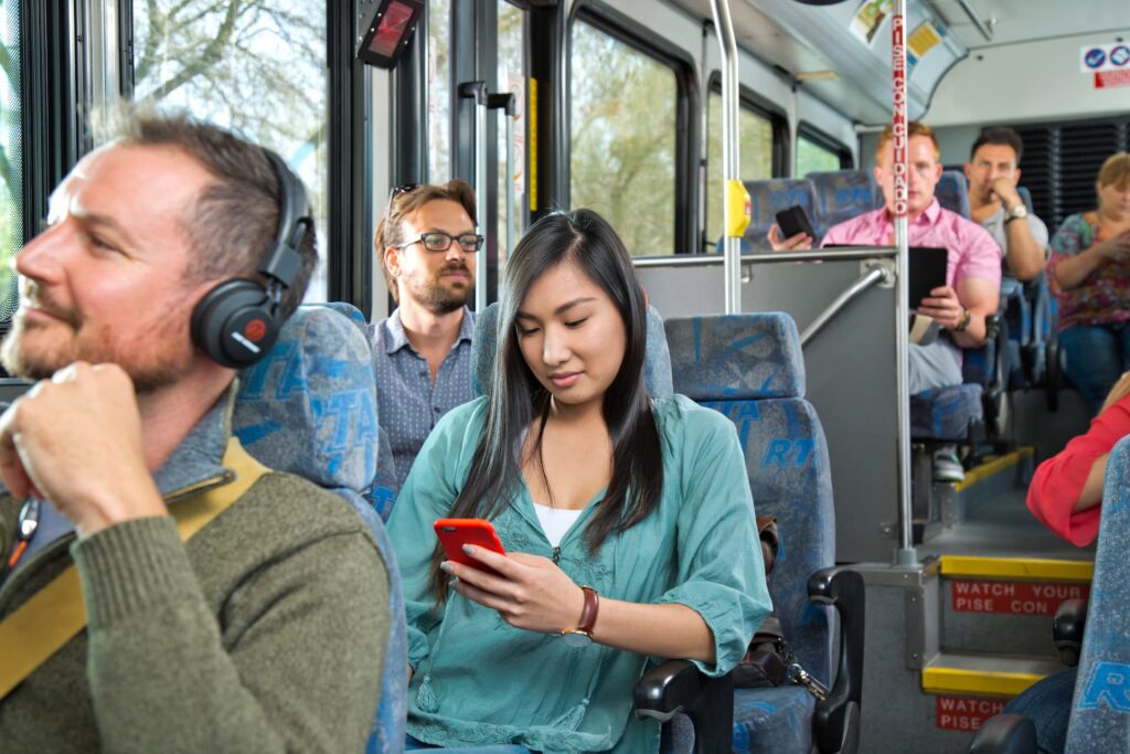Commuters ride on a bus, a woman looks down at her cell phone.